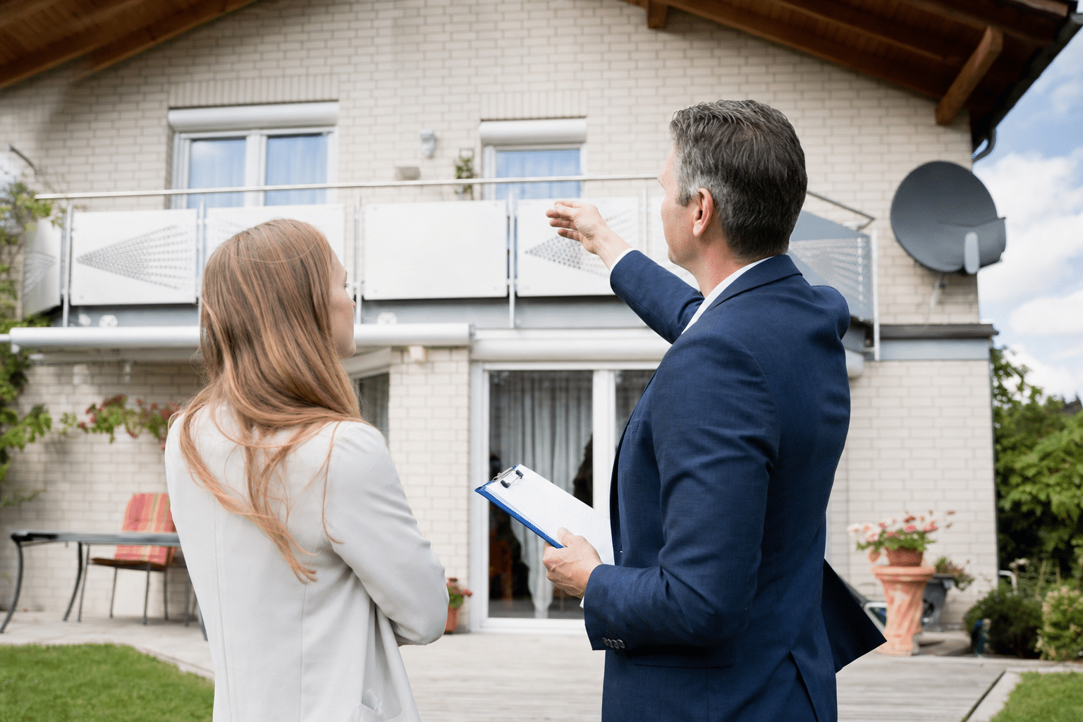 Sachverständiger prüft mit einer Eigentümerin die Fassade eines Einfamilienhauses